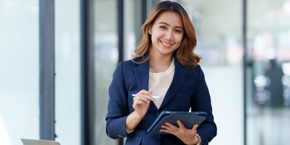 Smiling Professional Woman in Navy Blazer Holding Tablet and Stylus in Modern Office.