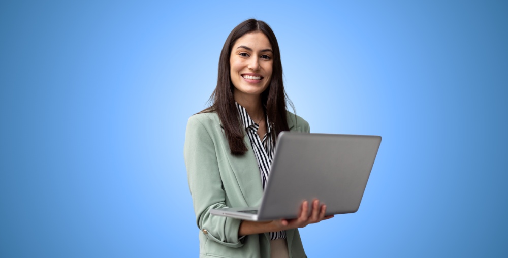 Smiling Woman in Green Blazer Holding Laptop on Blue Background.
