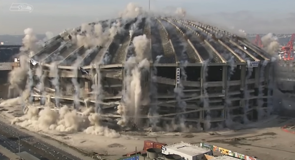 Large domed stadium implosion with massive dust clouds during demolition.