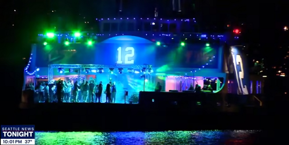Seattle Seahawks #12 party on ferry boat lit up at night with dancers.